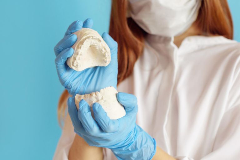 A female dentist holding a model of a tooth on a blue background.